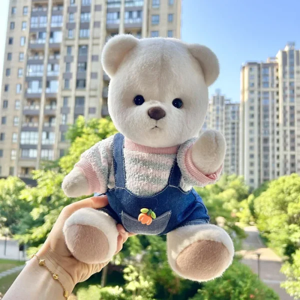l'ours en peluche blanc habillé en salopette en jeans est assis de face